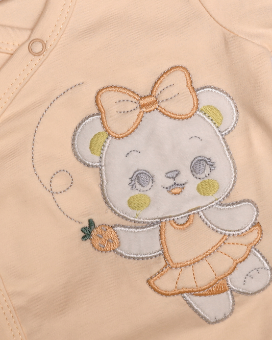 Close-up of embroidered ballerina bear with golden bow and carrot on peach baby top